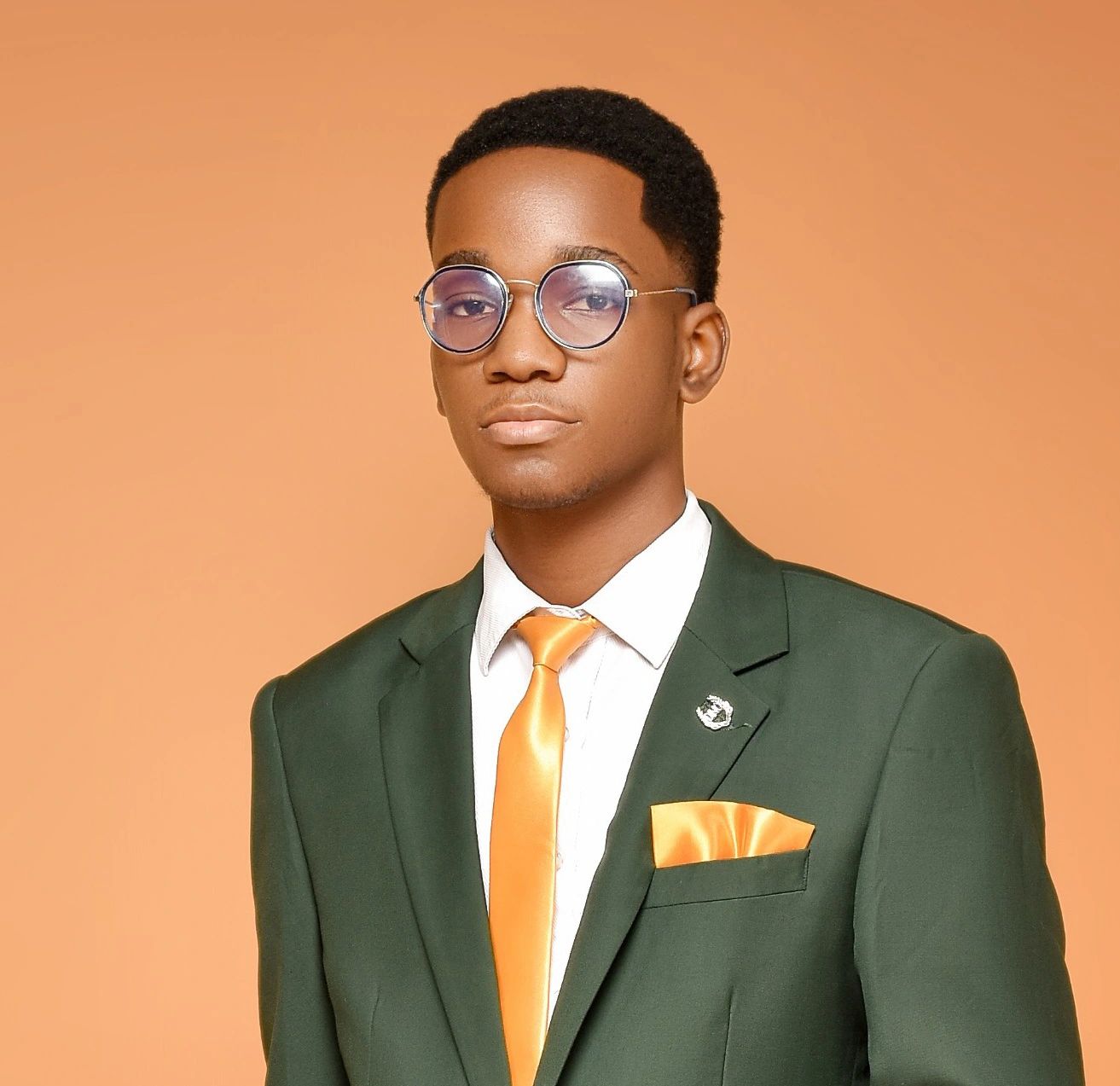 Portrait of Cross Makele in a green suit and gold tie against a warm orange backdrop